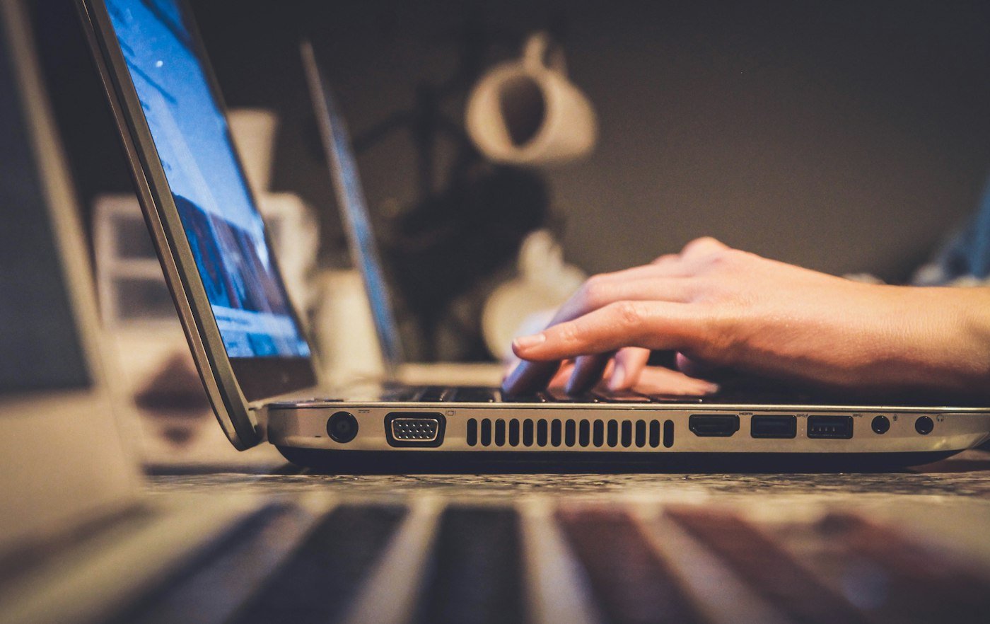 Bok laptopa z widocznymi gniazdami i dłoń na klawiaturze